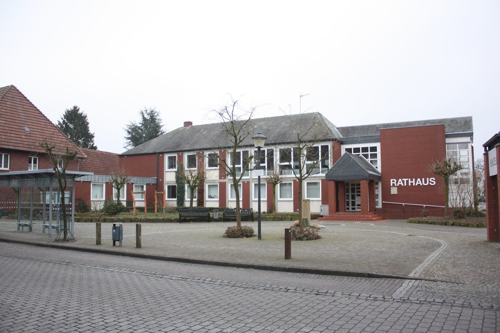 The town hall of Ostbevern, a red-brick building with the sign 'Rathaus', on an empty paved square.